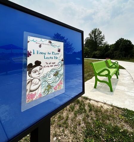 A panel from the Bronson Park Storywalk showing the title page for the book I Know the River Loves Me. A green bench is in the background.