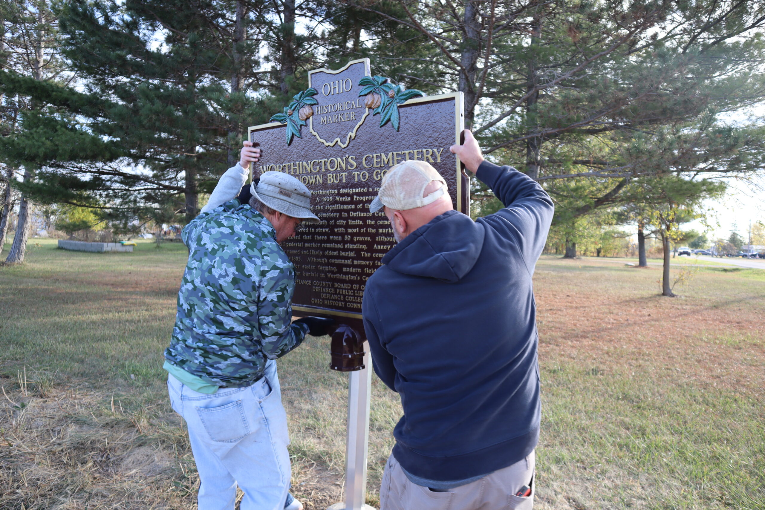 Two men lifting the Worthington Cemetery Ohio Historic Marker onto its post